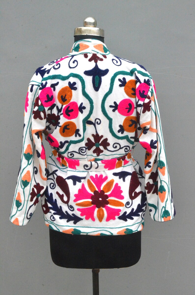 May include: White cotton jacket with colorful floral embroidery. The jacket has a belt and long sleeves.
