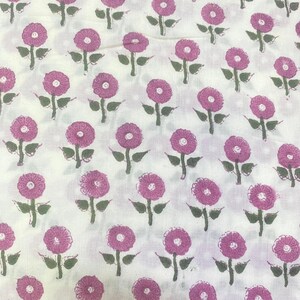 Op de afbeelding: Een witte stof met een herhalend patroon van kleine roze bloemen met donkergroene stengels en bladeren. Het bloemmotief is in een rasterachtig patroon over het oppervlak verdeeld, wat een consistente botanische print op het textiel laat zien.