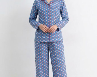 May include: Blue pajama set with a repeating cupcake pattern. The long-sleeved top has a collared neckline and pink trim. The matching pants are wide-legged. The pajamas are made of a soft fabric.