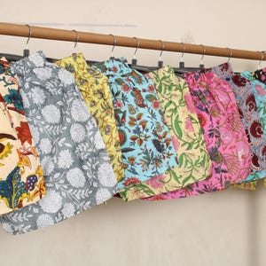 Puede incluir: Una colección de pantalones cortos de tela estampada de colores colgados en un estante. Los pantalones cortos están hechos de algodón y tienen una variedad de patrones florales y geométricos.