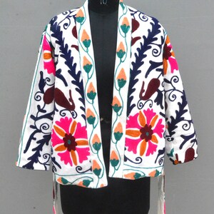 May include: White embroidered jacket with floral and paisley patterns in pink, orange, green, and blue. The jacket has a tie closure and long sleeves.