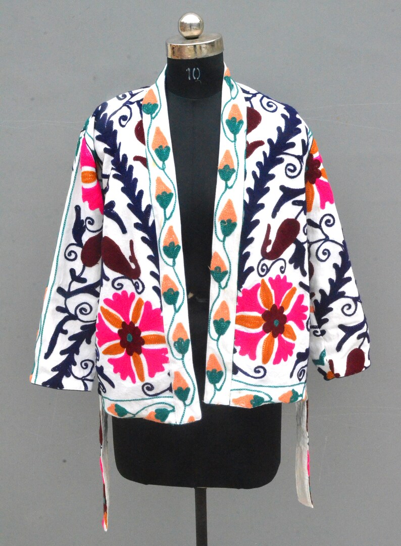 May include: White embroidered jacket with floral and paisley patterns in pink, orange, green, and blue. The jacket has a tie closure and long sleeves.