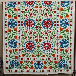 May include: White fabric with a colorful floral embroidery pattern. The design features blue, red, orange, and green flowers.