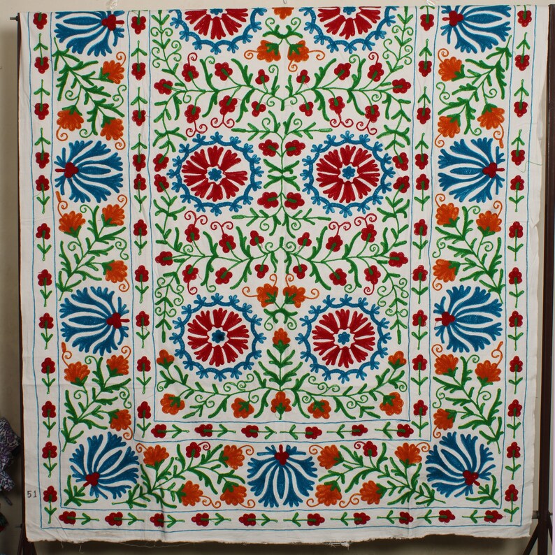 May include: White fabric with a colorful floral embroidery pattern. The design features blue, red, orange, and green flowers.