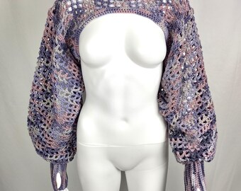 May include: A crocheted shrug in shades of lavender, pink, and gray. The open-weave design features long, voluminous sleeves with thumb holes and a cropped bodice. The garment is displayed on a white mannequin.