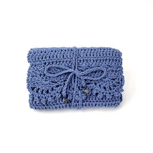 May include: A folded, crocheted clutch in a dusty blue hue. The handmade bag features a decorative openwork pattern and is secured with a matching cord tied in a bow. Two small, decorative beads are attached to the cord.