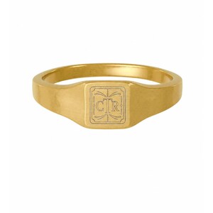 May include: A gold signet ring featuring a square face with rounded corners. The center of the face is engraved with the letters CTR inside a decorative border with thin lines and small flourishes at the top and bottom of the square frame.
