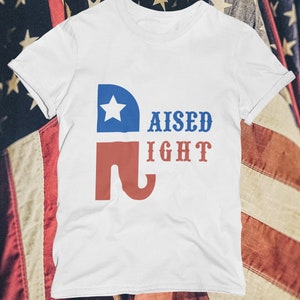 May include: White t-shirt with a red and blue elephant graphic and the text "RAISED RIGHT".