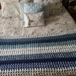 K&ouml;nnte beinhalten: Eine gestrickte blaue, wei&szlig;e und graue gestreifte Decke mit flauschigem Muster.