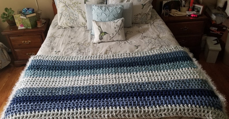 K&ouml;nnte beinhalten: Eine gestrickte blaue, wei&szlig;e und graue gestreifte Decke mit flauschigem Muster.