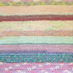 Könnte beinhalten: Eine mehrfarbige gehäkelte Decke mit Streifen in Pink, Lila, Blau, Grün und Weiß.