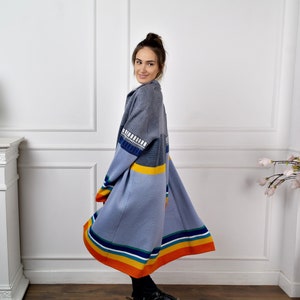 May include: A long, blue and gray cardigan with colorful stripes on the bottom and a geometric pattern on the sleeve. The cardigan is made of a soft, knitted fabric.