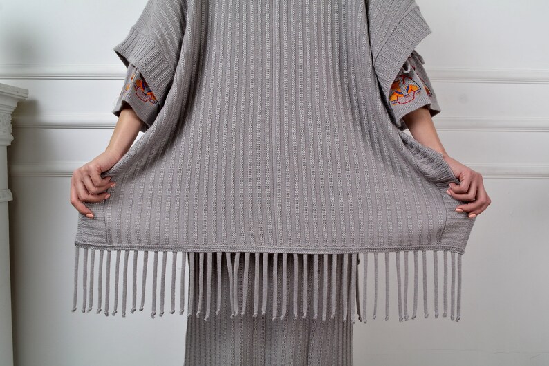 Op de afbeelding: Een grijze gebreide cardigan met een franje rand. De cardigan heeft geborduurde details op de mouwen.