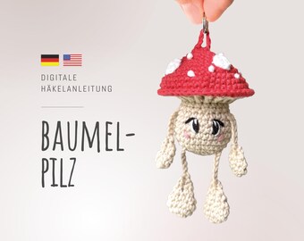 May include: A crocheted mushroom keychain with a red cap and white spots, beige stem, and dangling legs. The mushroom has a smiling face with black eyes and pink cheeks. The image includes the text "BAUMEL-PILZ" and "DIGITALE HÄKELANLEITUNG".