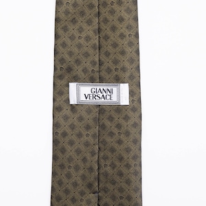 May include: A brown silk tie with a gold geometric pattern and a white label that reads "Gianni Versace".
