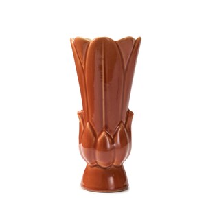 Puede incluir: Un jarrón de cerámica marrón con un diseño en forma de flor. El jarrón tiene una abertura ancha y una base estrecha.
