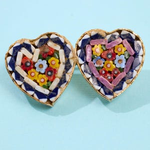 May include: Two heart-shaped mosaic earrings with gold-colored trim. The mosaic design features colorful flowers in red, yellow, blue, and purple. The earrings are set against a light blue background.