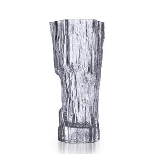 May include: A clear glass vase with a textured, bark-like exterior. The vase has a tall, cylindrical shape with a slightly irregular top edge. The glass appears to be thick and sturdy, suitable for holding flowers or decorative items.
