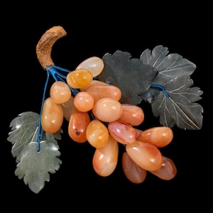 May include: A carved jade grapevine with a cluster of orange agate grapes. The grapes are carved in a realistic style and the leaves are detailed.
