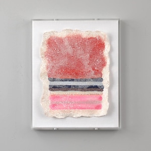 Puede incluir: Una pieza de arte abstracto enmarcada con un diseño en capas de color rojo, rosa y negro. La obra de arte está enmarcada en un marco transparente con un passe-partout blanco.