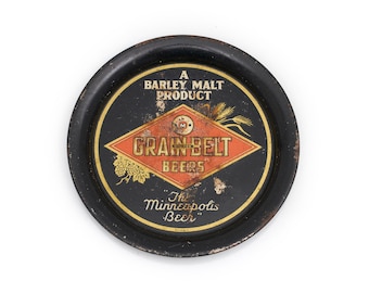 Könnte beinhalten: Ein runder, schwarzer Grain Belt Beers-Tablett mit goldenem Rand. In der Mitte befindet sich ein rautenförmiges Logo mit den Worten "Grain Belt Beers" und "The Minneapolis Beer". Das Tablett ist ein Gerstenmalzprodukt.