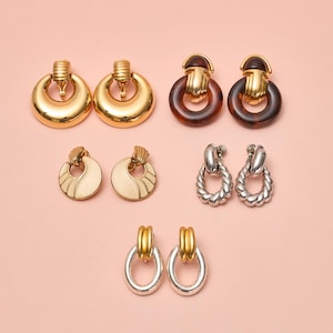 May include: Assortment of gold and silver tone earrings with various designs. The earrings feature a round shape with a knob-like detail. Some earrings have a tortoise shell design.