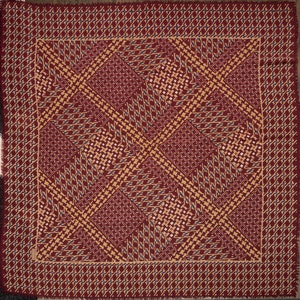 Puede incluir: Una bufanda cuadrada roja y dorada con un diseño geométrico. La bufanda tiene un borde con flecos.