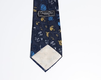 May include: A navy blue silk tie with a gold, blue, and white abstract pattern. The tie has a label that reads "Christian Dior Cravates Paris New York".
