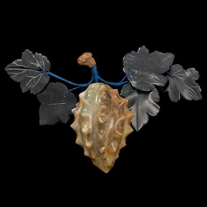 May include: A carved jade sculpture of a spiky fruit with leaves, the fruit is brown and yellow, the leaves are black, and the stem is blue.