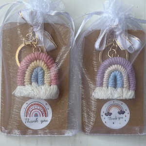 May include: Two rainbow keyrings in organza gift bags. The keyrings feature a macrame rainbow design in pastel colours, with a gold-coloured keyring. Each keyring is attached to a brown card with a "Thank you" sticker.