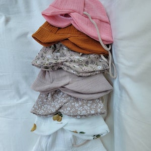 May include: A stack of five different sun hats. The top hat is pink, the second is brown, the third is beige with a floral pattern, the fourth is beige, and the bottom hat is white with a lemon pattern.