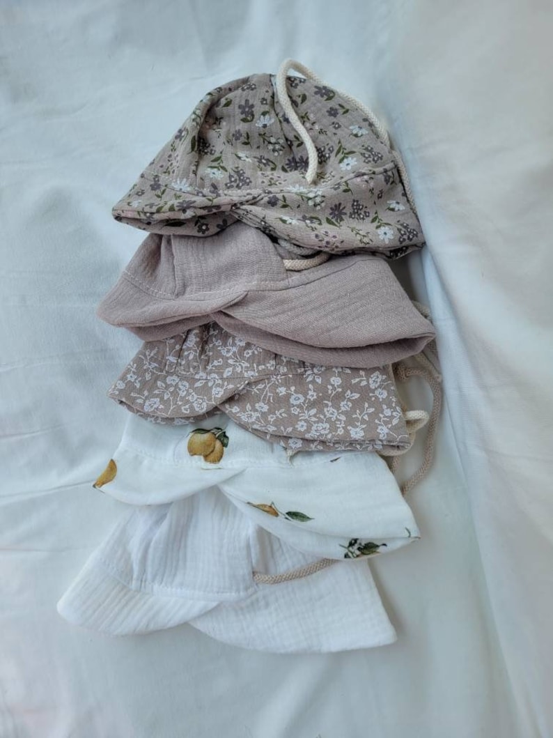 May include: A stack of four cotton sun hats with floral and lemon prints. The hats are in shades of white and beige.