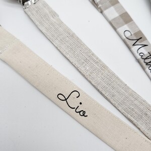May include: Three personalized pacifier clips with wooden beads and different fabric patterns. The clips are labeled "Lio", "Mathew", and "Noah".