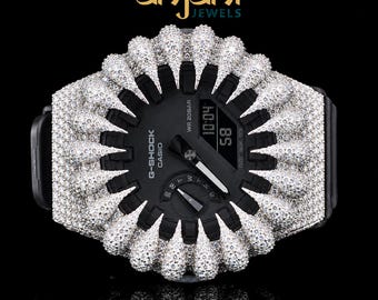 May include: A black G-Shock Casio watch featuring a custom bezel encrusted with numerous small, clear, sparkling stones arranged in a radial, spike-like pattern. The watch face displays the text G-Shock, Casio, and WR 20BAR with digital time 10:04.