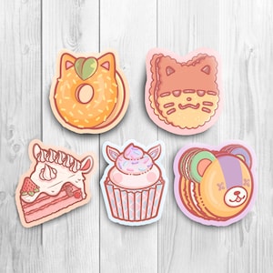 May include: Five colorful stickers featuring different animal-shaped desserts. The stickers include a donut with a cat face, a cookie with a cat face, a cupcake with a unicorn face, a cake slice with a unicorn face, and a macaron with a bear face.