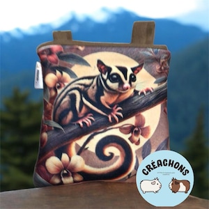 Puede incluir: Una bolsa decorativa con una ilustración de una ardilla voladora en una rama, rodeada de flores. La bolsa tiene una parte superior marrón y un logotipo circular con el texto "Créachons" y dos ilustraciones de animales.