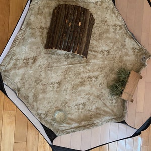 May include: A beige playpen with a brown wooden log hideaway, a small glass jar, and a pile of hay in a wooden box.