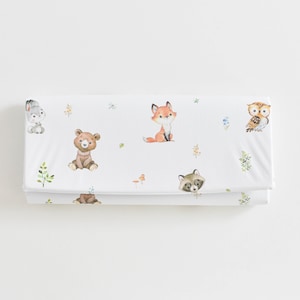 May include: White fabric featuring a repeating pattern of woodland creatures such as a fox, bear, owl, raccoon, and rabbit. The illustrations are in soft watercolour tones with green foliage and small flowers.