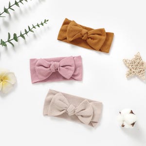 Könnte beinhalten: Drei Stoff-Haarband mit einer geknoteten Schleife. Die Haarband sind in beige, rosa und braun.