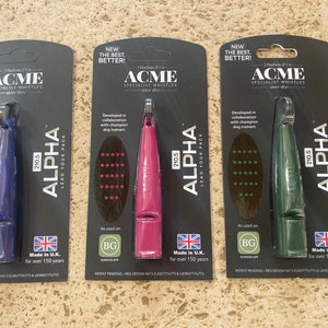 Könnte beinhalten: Drei Hundepfeifen in blauer, rosa und grüner Verpackung. Jede Pfeife ist mit "210.5 Alpha" und "Lead Your Pack" beschriftet. Die Verpackung weist auch auf "Neu Das Beste, Besser!" und "Hergestellt in Großbritannien seit über 150 Jahren" hin.