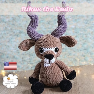 May include: A handmade crochet kudu plush toy. The plush features a brown body, black hooves, and large, dark eyes. The kudu has white markings on its face and purple and gray horns. The text "Rikus the Kudu" is displayed above the plush.