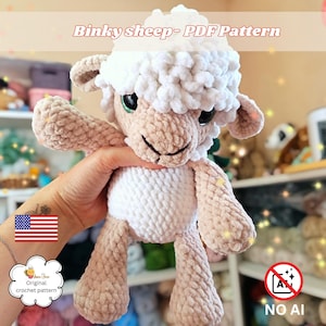 Puede incluir: Un juguete de oveja tejido a ganchillo con una cabeza de lana blanca texturizada y un cuerpo de color tostado claro. La oveja tiene ojos oscuros grandes, una nariz bordada y orejas caídas. El texto Binky sheep- PDF Pattern es visible.
