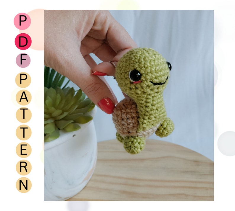 May include: A green crocheted turtle with a brown shell and black eyes. The turtle is being held by a hand.
