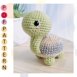 May include: A crocheted green turtle with a brown and gray shell. The turtle has black eyes and a pink mouth.