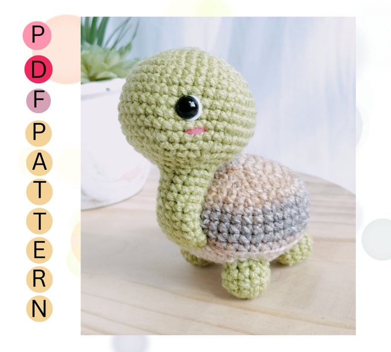 May include: A crocheted green turtle with a brown and gray shell. The turtle has black eyes and a pink mouth.