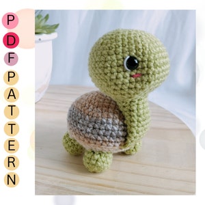May include: A crocheted green turtle toy with brown and gray stripes on its shell. The turtle has a black eye and a pink mouth.