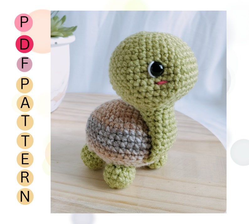 May include: A crocheted green turtle toy with brown and gray stripes on its shell. The turtle has a black eye and a pink mouth.