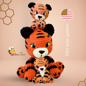 May include: Three crocheted tiger plushies stacked on top of each other. The largest tiger is orange and black with a white face. The middle tiger is orange and black with a white face. The smallest tiger is orange and black with a white face. The tigers are sitting on a peach background with a honeycomb pattern.