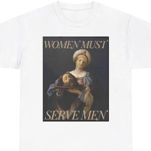 Pode incluir: Uma camiseta branca com uma estampa gráfica de uma mulher segurando uma cabeça decepada em uma tigela. O texto "WOMEN MUST SERVE MEN" está impresso em letras marrons no gráfico.