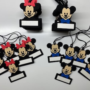 May include: A set of 10 black felt Mickey Mouse and Minnie Mouse character name tags with black string. Each tag has a blank white space for writing a name. The Minnie Mouse tags have red bows and the Mickey Mouse tags have blue bow ties.